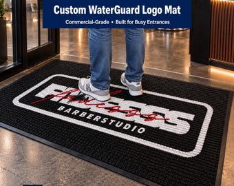 May include: A rectangular black floor mat with a textured surface and a white border. The center features the white text "FADEZ" in a bold font with a red script overlay, and the word "BARBERSTUDIO" in white capital letters below it.