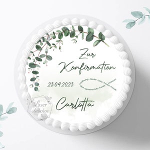 Könnte beinhalten: Ein runder weißer Kuchen, verziert mit grünen Eukalyptusblättern und dem Text "Zur Konfirmation" und dem Datum "23.04.2023". Der Name "Carlotta" ist ebenfalls abgebildet. Der Kuchen hat einen weißen Zuckergussrand.