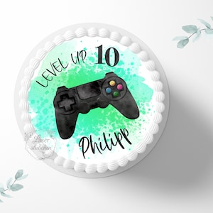 Könnte beinhalten: Ein runder Kuchen mit einer weißen Frosting-Basis und einem grün-blauen Aquarell-Design. Das Design zeigt einen schwarzen Videospiel-Controller und den Text "LEVEL UP 10 Philipp".