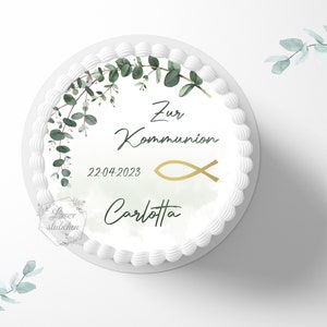 Könnte beinhalten: Weißer Kuchen mit grünen Eukalyptusblättern und einem goldenen Fischsymbol. Der Kuchen ist mit dem Text "Zur Kommunion", "22.04.2023" und "Carlotta" verziert.