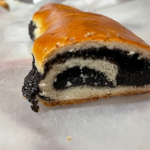May include: A poppy seed roll with a dark filling, sliced in half and showing the inside. The roll is on a white parchment paper.