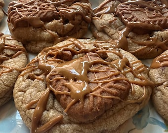 May include: Close-up of several large, round cookies on a decorative plate. The cookies are light brown with a drizzle of caramel sauce and a cookie on top. The plate has a blue and white checkered pattern.