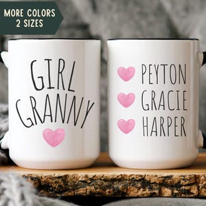 May include: Two white ceramic mugs with black handles. One mug says "Girl Granny" with a pink heart. The other mug says "Peyton Gracie Harper" with three pink hearts.