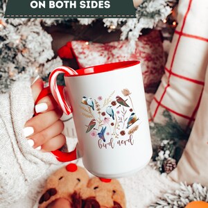 May include: White ceramic mug with a red rim and handle. The mug features a colorful illustration of birds and flowers with the text "bird nerd" in pink lettering.