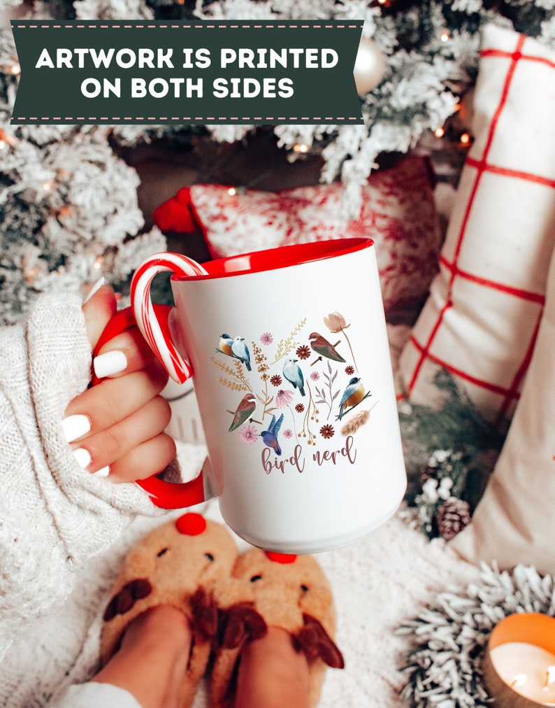 May include: White ceramic mug with a red rim and handle. The mug features a colorful illustration of birds and flowers with the text "bird nerd" in pink lettering.