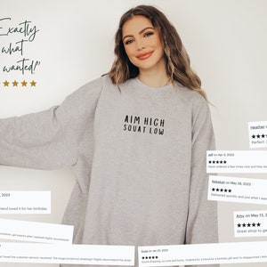 May include: A grey sweatshirt with the text "AIM HIGH SQUAT LOW" printed on the front. The sweatshirt is being modelled by a person. The image includes customer reviews with five stars and positive comments.