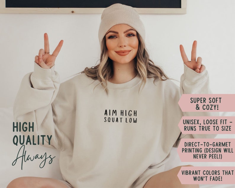 May include: A beige sweatshirt with the text "AIM HIGH SQUAT LOW" printed on the front. The sweatshirt is super soft and cosy, unisex, and runs true to size. It is made with direct-to-garment printing, so the design will never peel. The sweatshirt is available in vibrant colours that won't fade.