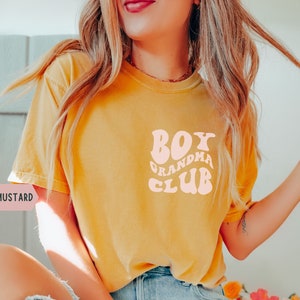 May include: A mustard yellow t-shirt with a pink graphic that says "Boy Grandma Club" in a retro font.