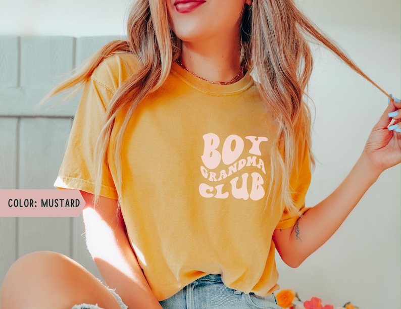 May include: A mustard yellow t-shirt with a pink graphic that says "Boy Grandma Club" in a retro font.