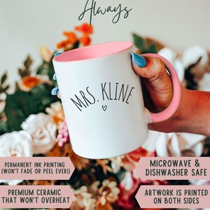 May include: White ceramic mug with a pink interior and handle, featuring the text "MRS. KLINE" in black script. The mug is held in a hand with blue nail polish, with the words "HIGH QUALITY Always" at the top.
