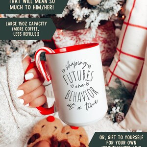 May include: White ceramic mug with a red interior and handle, featuring the text "shaping FUTURES one BEHAVIOR at a time." A candy cane rests on the rim. The mug has a 150z capacity. The image includes text that says "A unique & special gift" and "Gift to yourself."