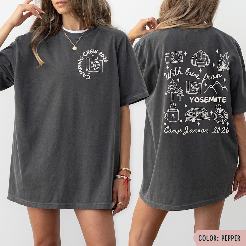 K&ouml;nnte beinhalten: Dunkelgraues T-Shirt mit wei&szlig;en Camping-Motiven. Auf der Vorderseite steht "Camping Crew 2026" und eine Karte. Auf der R&uuml;ckseite befinden sich Illustrationen und der Text: "With love from Yosemite, Camp Janson 2026."