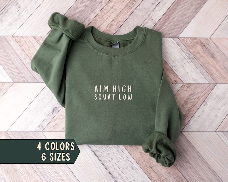 May include: A green sweatshirt with the text "AIM HIGH SQUAT LOW" in white lettering.