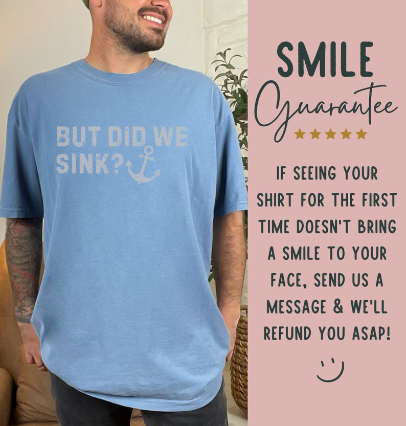 May include: A light blue t-shirt with the text "BUT DID WE SINK?" and an anchor graphic. The text is in a white distressed font. The t-shirt is being worn by a person. The image also includes a pink background with the text "SMILE Guarantee" and five stars.