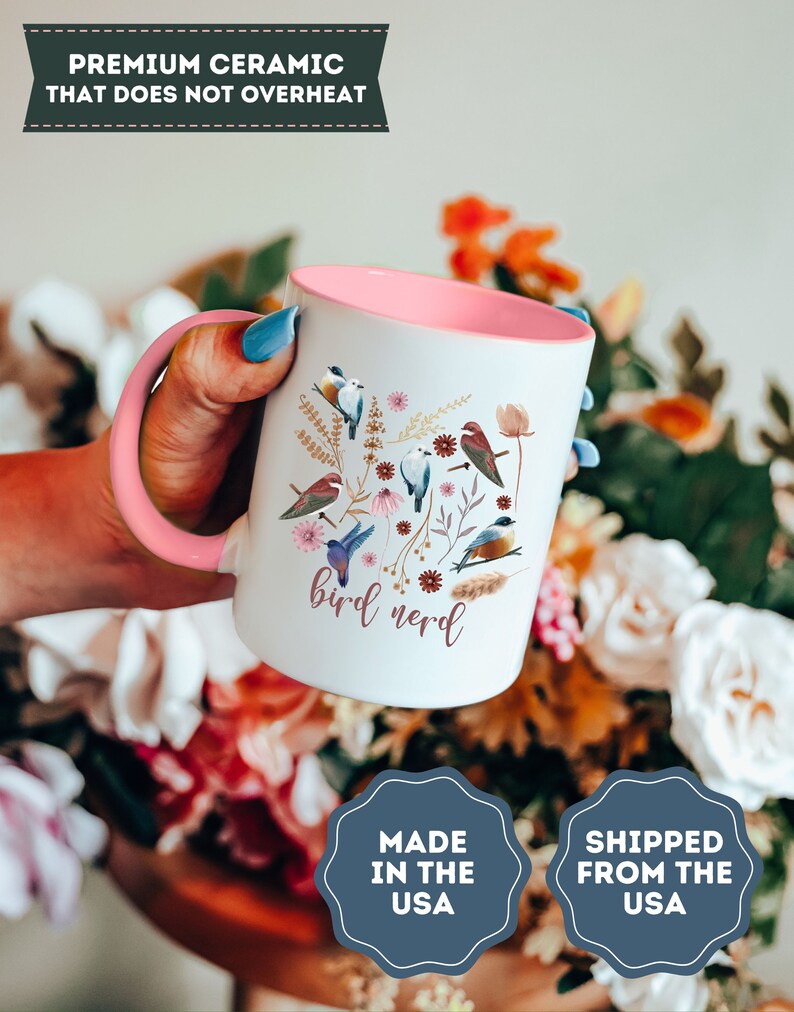 May include: White ceramic mug with a pink rim and handle. The mug features a colorful illustration of birds and flowers with the text "bird nerd".