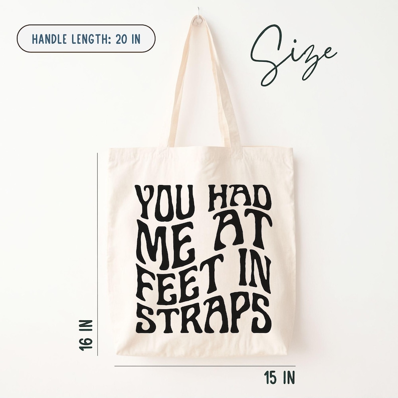 Puede incluir: Bolso tote color crema con texto negro "YOU HAD ME AT FEET IN STRAPS". El bolso mide 40,6 cm de alto, 38,1 cm de ancho y tiene una longitud de asa de 50,8 cm.
