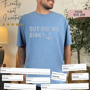 May include: A light blue t-shirt featuring the text "BUT DID WE SINK?" and an anchor graphic. The shirt is made from a soft, comfortable material and has a relaxed fit. The text is in a distressed white font. The anchor is white. The shirt is modelled on a person. The background is a blurred image of a plant and a lamp.