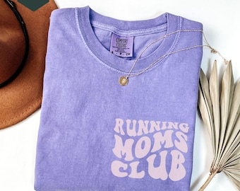 May include: Purple t-shirt with the text "Running Moms Club" in a retro font. The shirt is made of a soft, comfortable material.