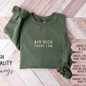 May include: A green sweatshirt with the text "AIM HIGH SQUAT LOW" printed on the front. The sweatshirt is super soft and cosy, with a unisex, loose fit that runs true to size. The design is printed directly onto the garment, so it will never peel. The vibrant colours won't fade.
