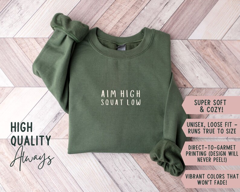 May include: A green sweatshirt with the text "AIM HIGH SQUAT LOW" printed on the front. The sweatshirt is super soft and cosy, with a unisex, loose fit that runs true to size. The design is printed directly onto the garment, so it will never peel. The vibrant colours won't fade.