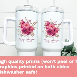 Puede incluir: Dos tazas aisladas blancas con asas, cada una adornada con un dise&ntilde;o floral en tonos rosas y marrones. El texto "Mrs. Johnson EST. 2026" est&aacute; impreso debajo de las flores. Las tazas tienen una tapa transparente y una pajita.