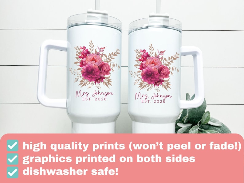Puede incluir: Dos tazas aisladas blancas con asas, cada una adornada con un dise&ntilde;o floral en tonos rosas y marrones. El texto "Mrs. Johnson EST. 2026" est&aacute; impreso debajo de las flores. Las tazas tienen una tapa transparente y una pajita.