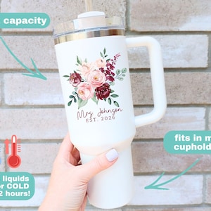 Puede incluir: Vaso t&eacute;rmico blanco con asa, decorado con un dise&ntilde;o floral en tonos rosas y burdeos. El vaso tiene una capacidad de 1,18 litros y el texto "Mrs. Johnson EST. 2026". Mantiene los l&iacute;quidos calientes o fr&iacute;os durante unas 12 horas.