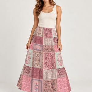 May include: A cream-colored ribbed tank top paired with a floor-length maxi skirt featuring a multi-paneled patchwork design. The skirt displays various floral and geometric patterns in shades of dusty rose, muted pink, sage green, and soft beige.