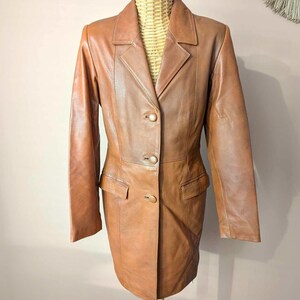 May include: A brown leather blazer with a classic design. The blazer features a notched collar, two front pockets, and three button closure. The jacket is displayed on a mannequin.