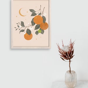 May include: A framed print with a minimalist illustration of an orange tree branch with oranges, leaves, and white flowers. The background is a light peach color with a crescent moon and gold stars.