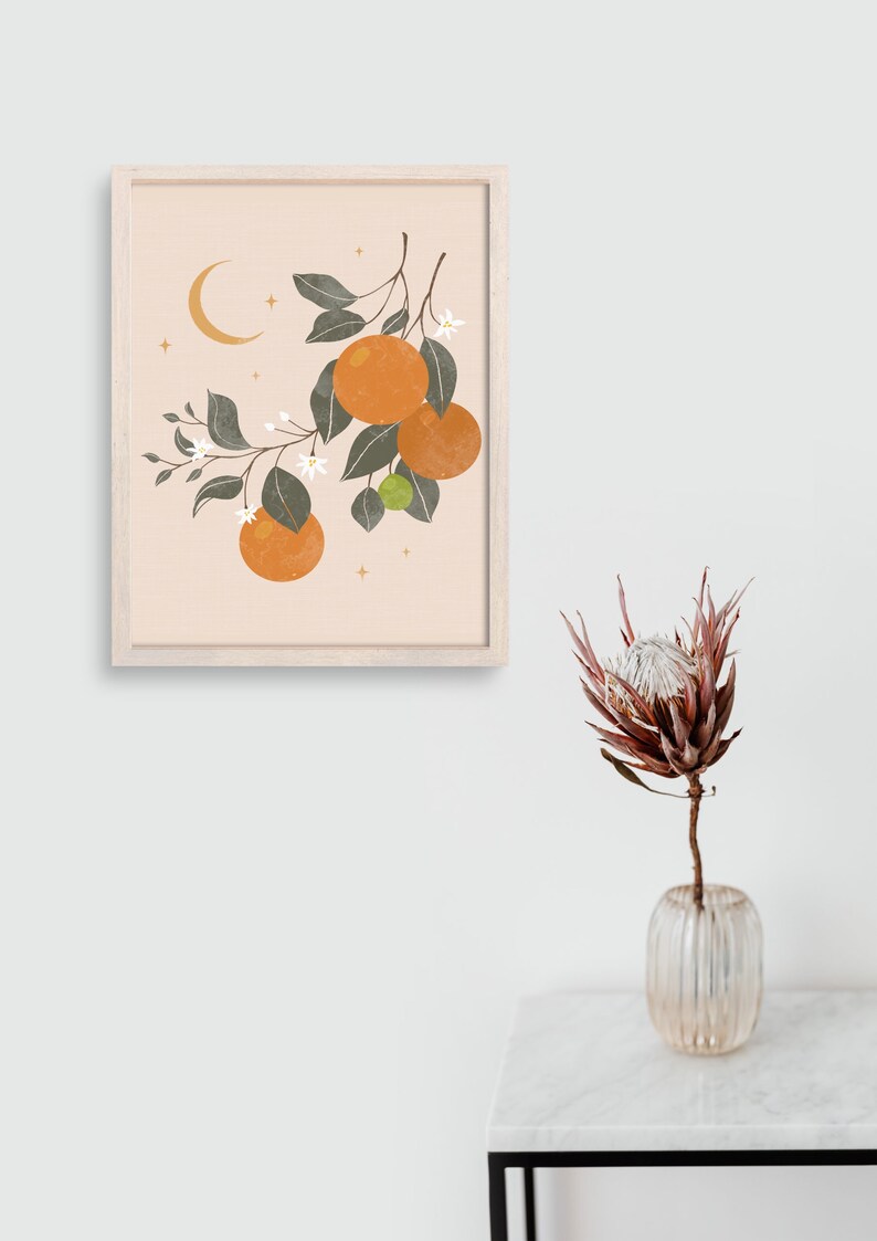 May include: A framed print with a minimalist illustration of an orange tree branch with oranges, leaves, and white flowers. The background is a light peach color with a crescent moon and gold stars.