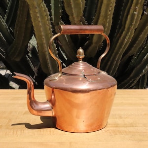May include: A copper kettle with a brass handle and spout. The kettle has a tarnished finish and a small knob on the lid.