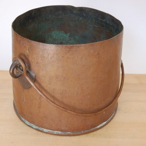 May include: A copper bucket with a single handle. The bucket is tarnished and has a green patina inside.