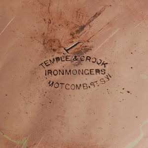 May include: Close-up of a copper pot with the inscription "Temple & Crook Ironmongers, Mottcomb, St. S.W."