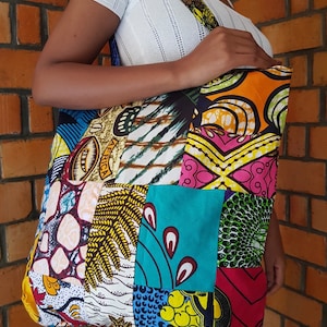 May include: A large patchwork tote bag with a variety of colorful African print fabrics. The bag has a long strap and is made of cotton.