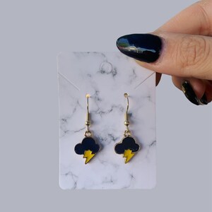 May include: A pair of gold dangle earrings with a black cloud and yellow lightning bolt charm.