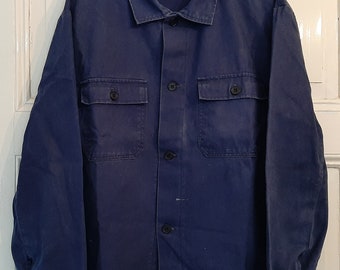 May include: A dark blue work shirt with long sleeves, a button-up front, and two large pockets on the chest. The shirt has a label that reads "Schulz & Kuster".