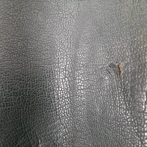 May include: Close-up of a dark gray textured leather surface with a small tear in the center.
