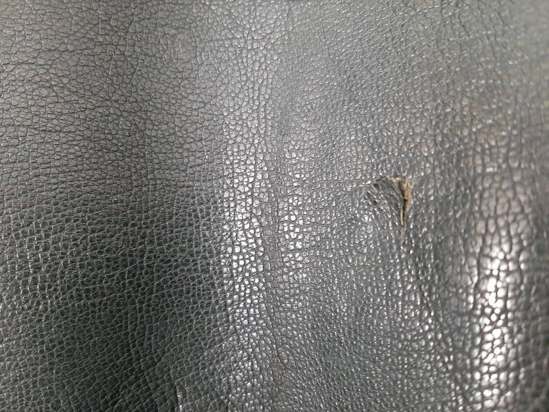 May include: Close-up of a dark gray textured leather surface with a small tear in the center.