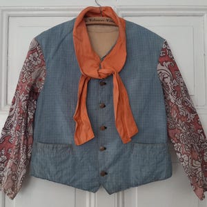 May include: A blue denim vest with a patterned fabric on the sleeves. The vest has a button-up front and a large orange scarf tied around the neck.