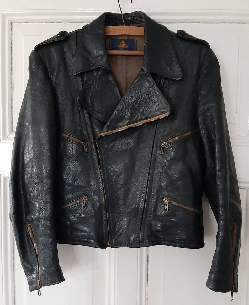 May include: A dark green leather motorcycle jacket with a zipper closure and multiple pockets. The jacket has a label with the text "ATF" inside a triangle.