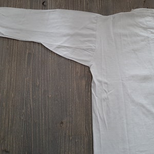 Op de afbeelding: Een wit overhemd met lange mouwen en een knoopsluiting. Het shirt ligt plat op een houten oppervlak.