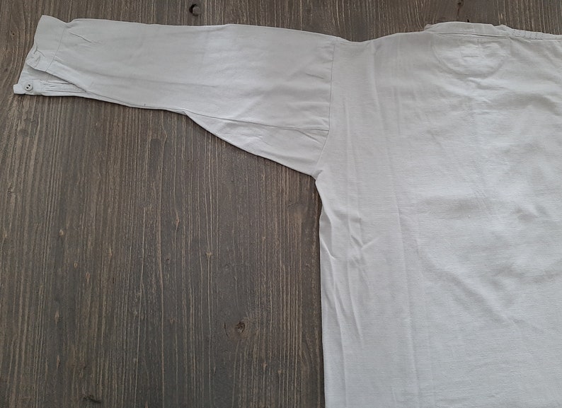 Op de afbeelding: Een wit overhemd met lange mouwen en een knoopsluiting. Het shirt ligt plat op een houten oppervlak.