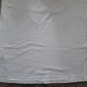 Op de afbeelding: Een effen wit T-shirt met een kleine scheur in de rechterbenedenhoek.