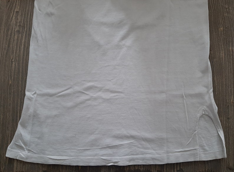 Op de afbeelding: Een effen wit T-shirt met een kleine scheur in de rechterbenedenhoek.