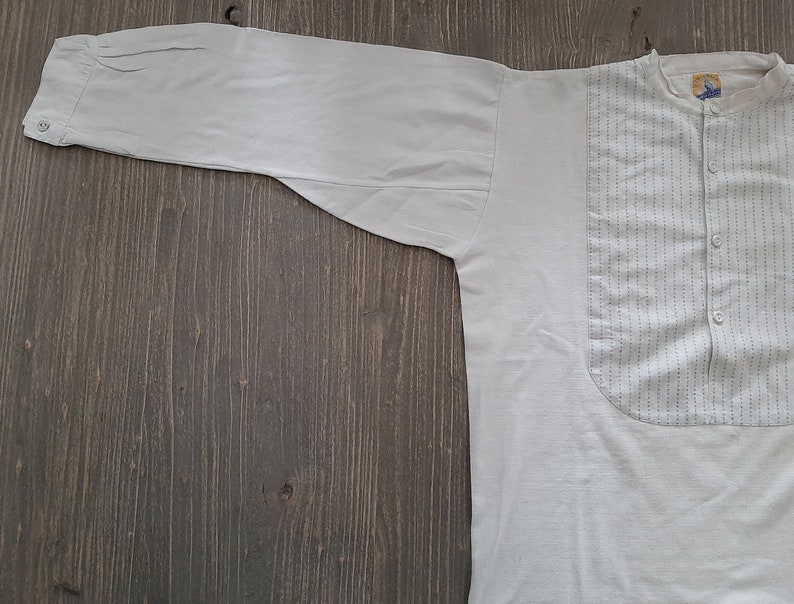 Op de afbeelding: Een wit overhemd met lange mouwen, een knoopsluiting en een klein zakje op de borst. Het zakje heeft een klein, donkerblauw patroon.