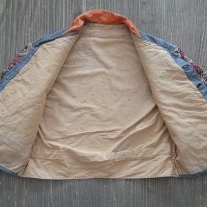 May include: A blue and red paisley patterned jacket with a light brown lining. The jacket is unbuttoned and laid flat on a wooden surface.