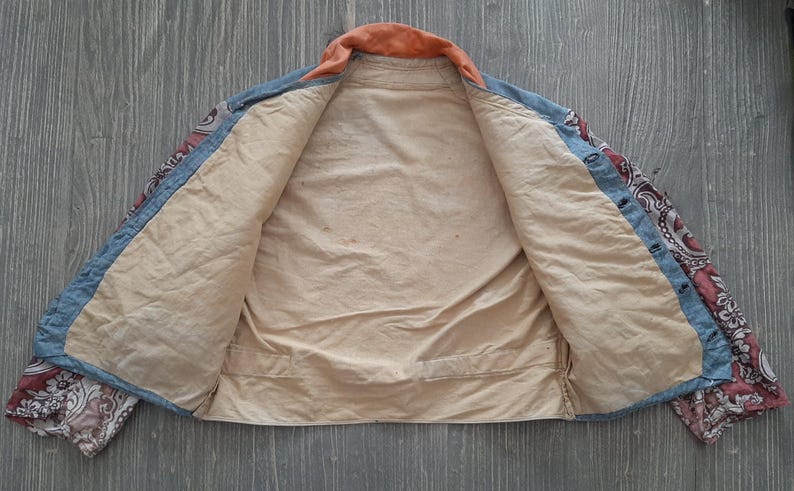 May include: A blue and red paisley patterned jacket with a light brown lining. The jacket is unbuttoned and laid flat on a wooden surface.