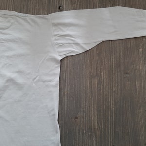 Op de afbeelding: Een effen wit overhemd met lange mouwen, plat gelegd op een houten oppervlak.