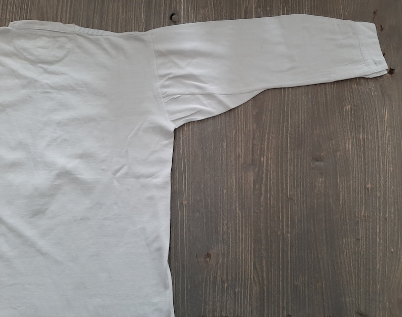 Op de afbeelding: Een effen wit overhemd met lange mouwen, plat gelegd op een houten oppervlak.